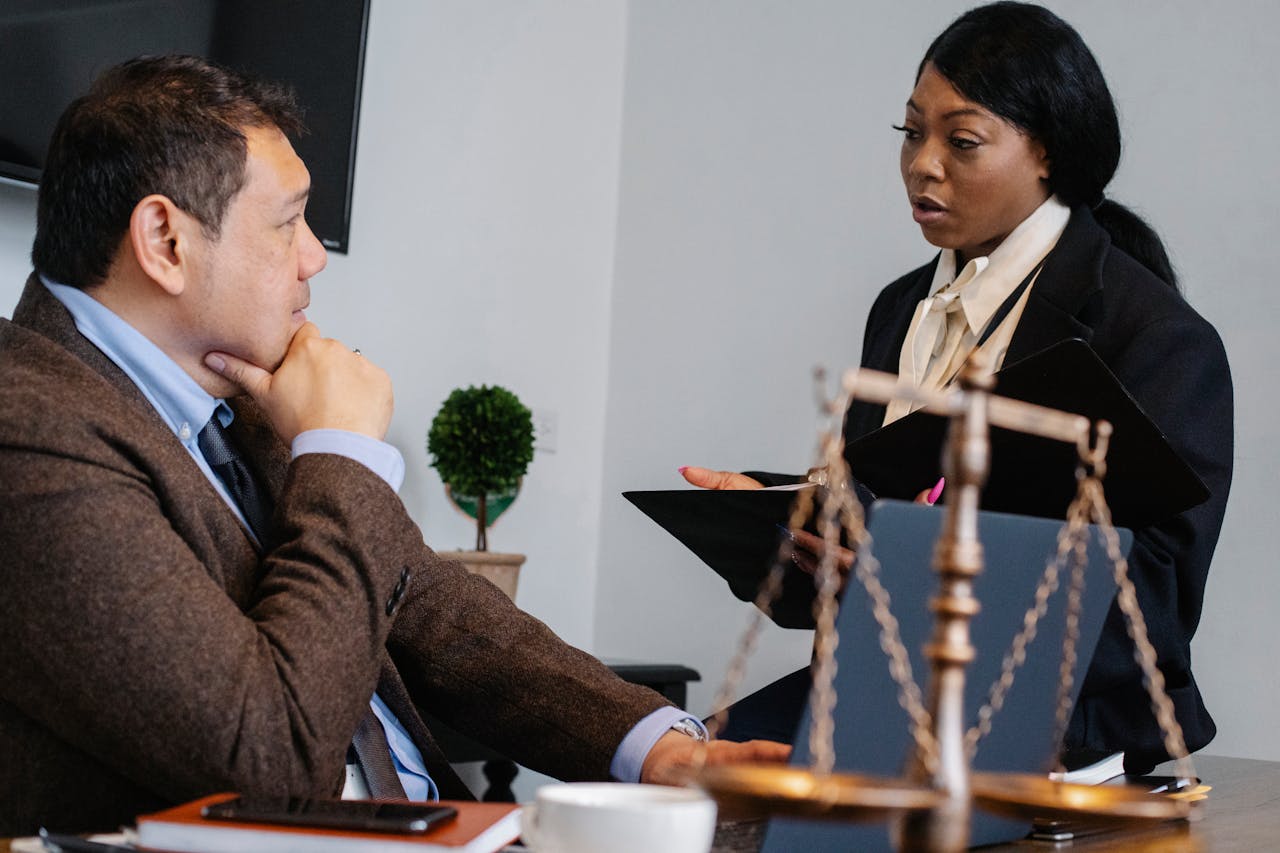 Side view of pensive diverse colleagues in formal clothes sitting at table and discussing details of project at work